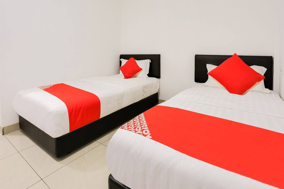 Two beds with black headboards and red pillows, white bedding, and a red and white patterned blanket.