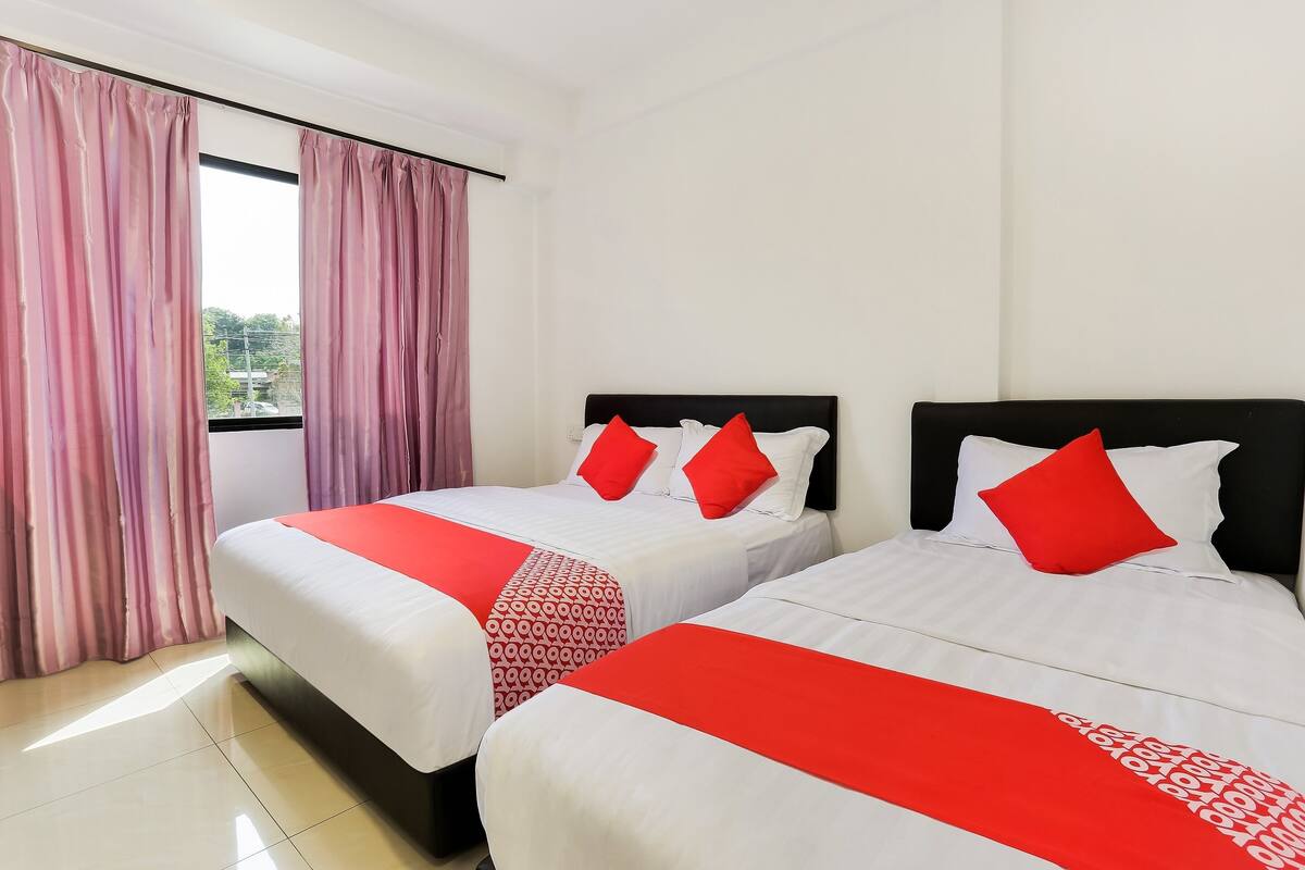 A hotel room with two beds, each with red and white bedding, and a large window with pink curtains.
