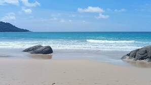 A beach with clear blue water, sandy shore, and large rocks.