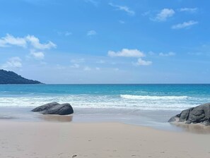 A beach with clear blue water, sandy shore, and large rocks. - Kata Gardens 4B Seaview Near Kata Noi (Karon)