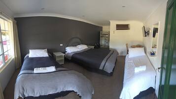 A hotel room with two beds, a window with curtains, a green door, and a small desk with a mirror.