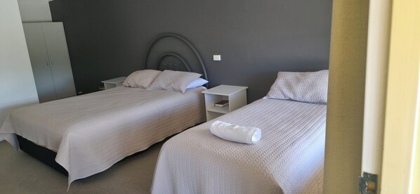 Un dormitorio con dos camas, cada una con cubrecama y almohadas blancas, cabecera gris y mesita de noche blanca.