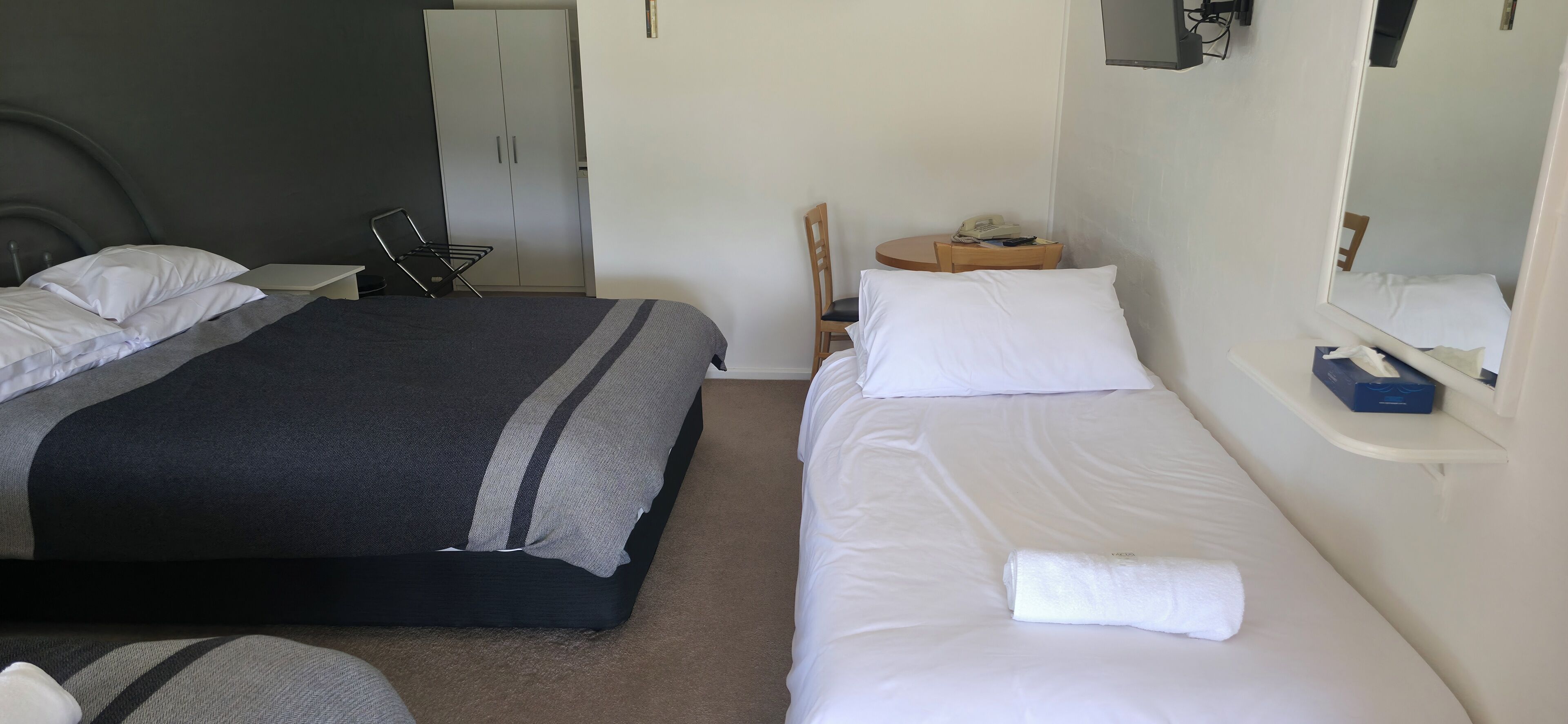 A hotel room with a bed, a desk, a chair, a wardrobe, and a mirror.