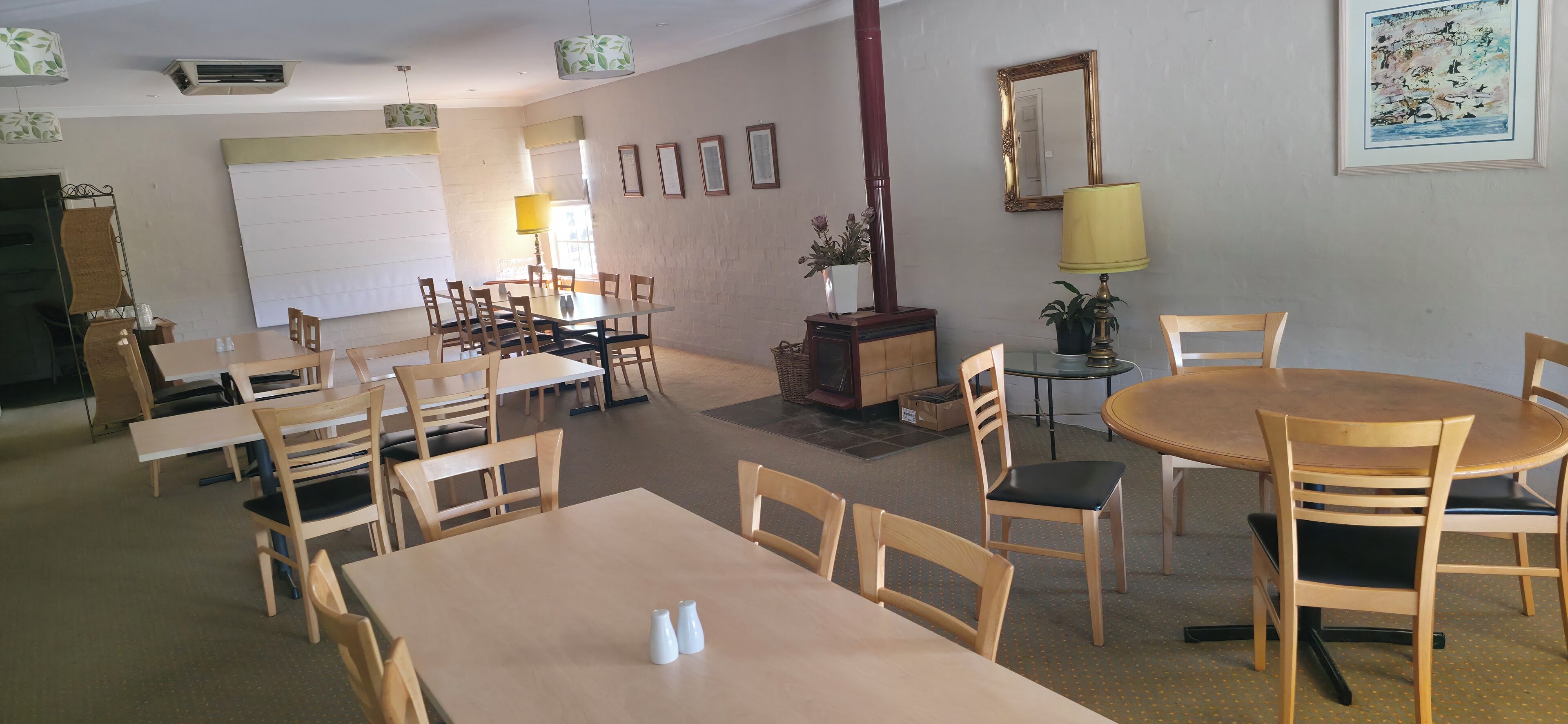 A dining area with multiple tables and chairs, a mirror, framed pictures, and a potted plant.