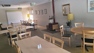 A dining area with multiple tables and chairs, a mirror, framed pictures, and a potted plant.