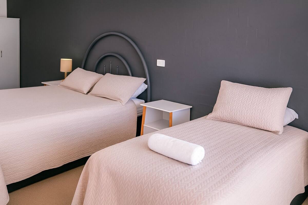 Quarto de hotel com duas camas, cada uma com cabeceira e mesa de cabeceira.