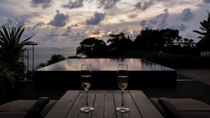 Two glasses of water on a wooden table with a view of the ocean and sky. - Kata Gardens Rooftop Plunge Pool Penthouse 4C (Karon)