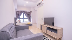 Ein modernes Wohnzimmer mit grauem Sofa, einem Fernseher auf einem Holzschrank, einem Bett mit Blick aus dem Fenster und einer Klimaanlage.