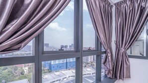 Ein Zimmer mit großen Fenstern und Vorhängen, das einen Blick auf eine Stadt mit Gebäuden und Grünflächen bietet.
