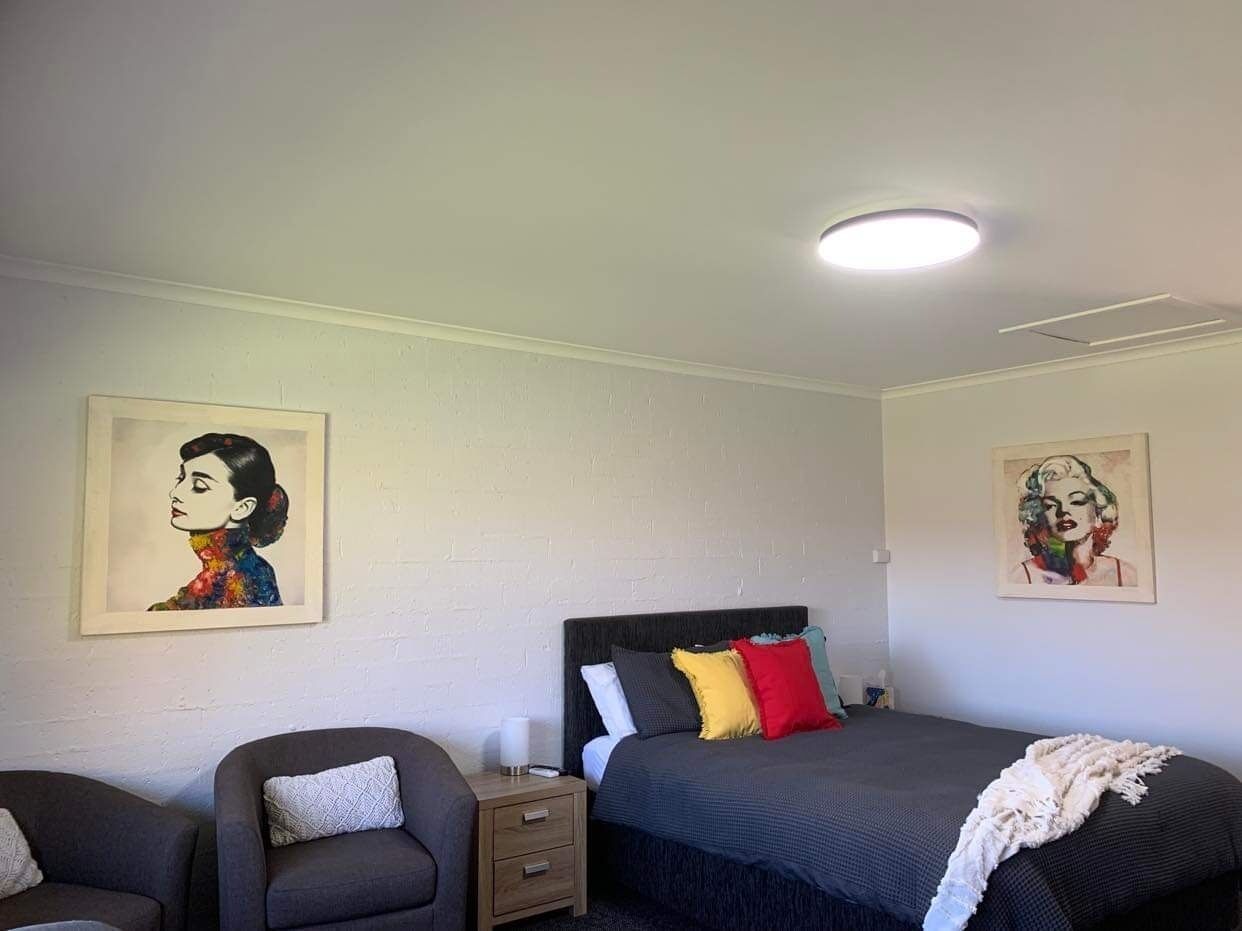 A bedroom with a bed, a chair, a nightstand, and two paintings on the walls.