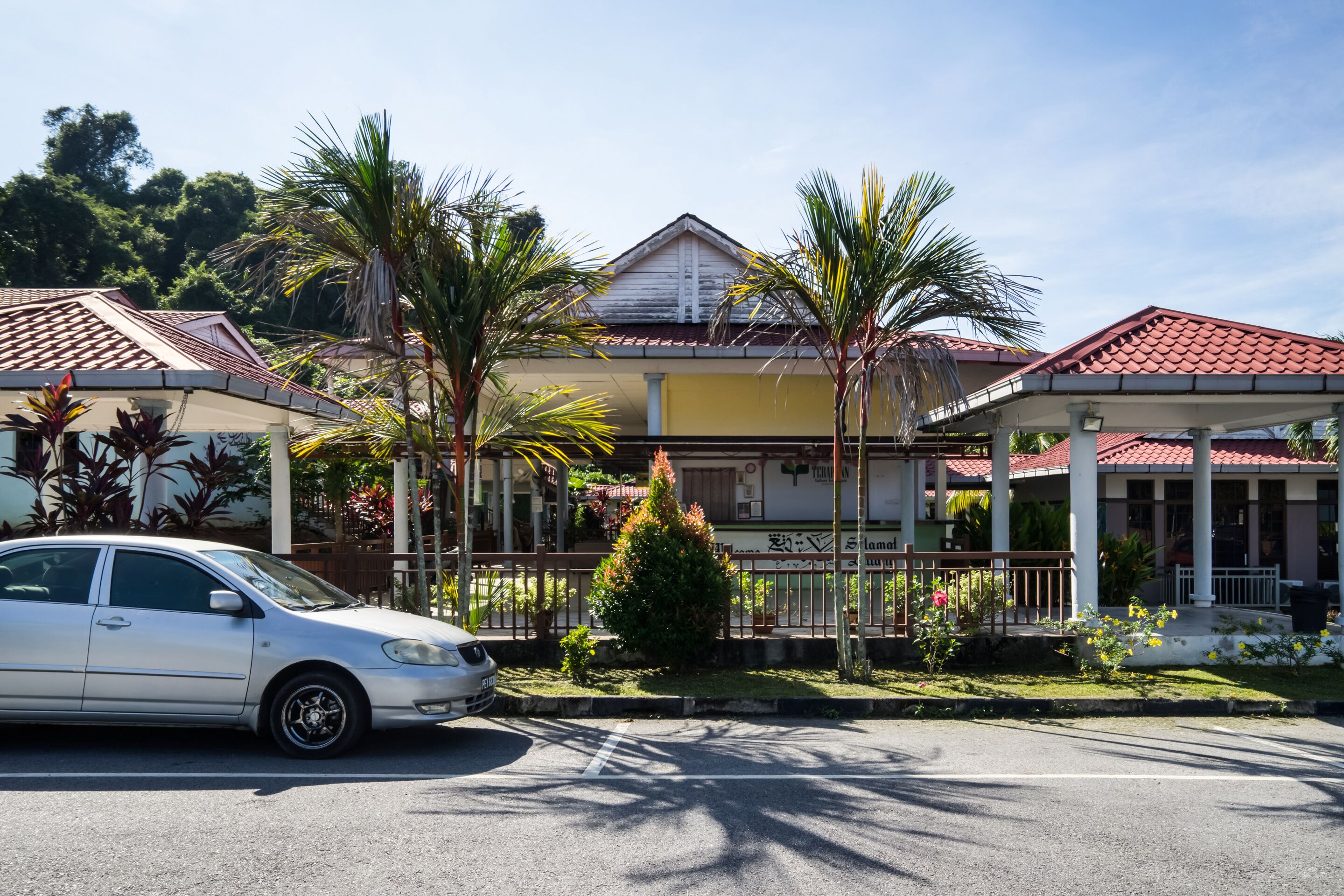 A building with a red-tiled roof, a covered porch, and a small tree in front.