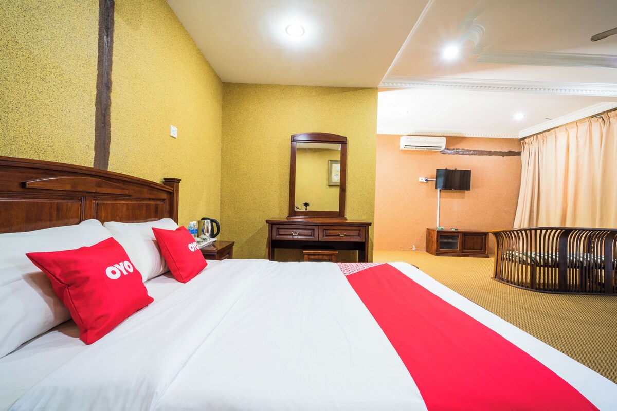 Une chambre d’hôtel avec un grand lit, une tête de lit en bois, une commode, un miroir, une télévision et un berceau.