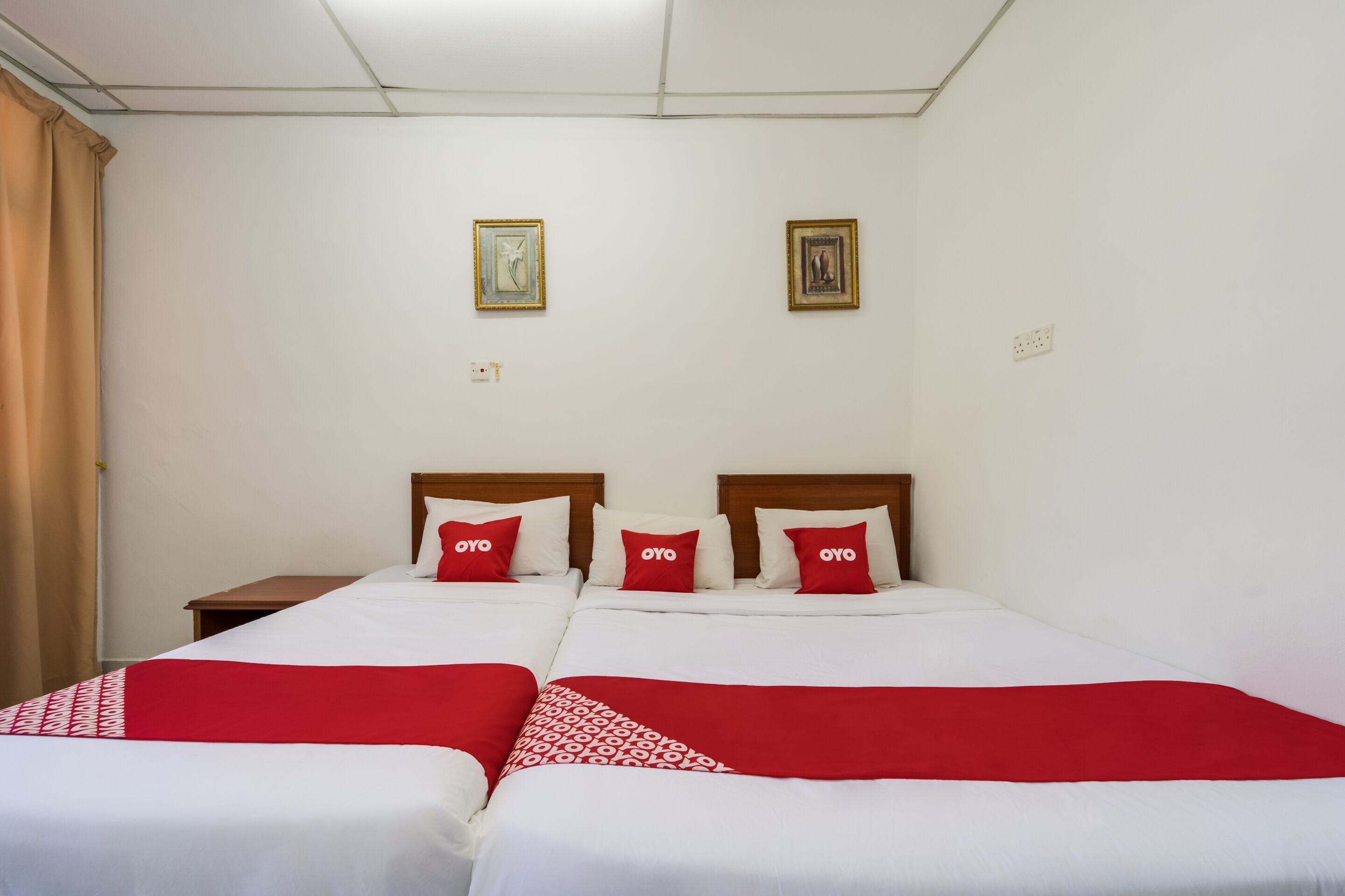 Une chambre d’hôtel avec deux lits, chacun doté de draps blancs et de touches de couleur rouge, d’une tête de lit en bois et d’une table de chevet.