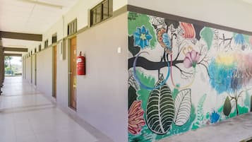 A corridor with a mural of colorful flowers and leaves on the wall, a fire extinguisher, and doors along the hallway.