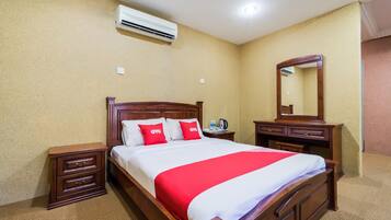 A hotel room with a wooden bed, a nightstand, a dresser, a mirror, and an air conditioning unit on the wall.