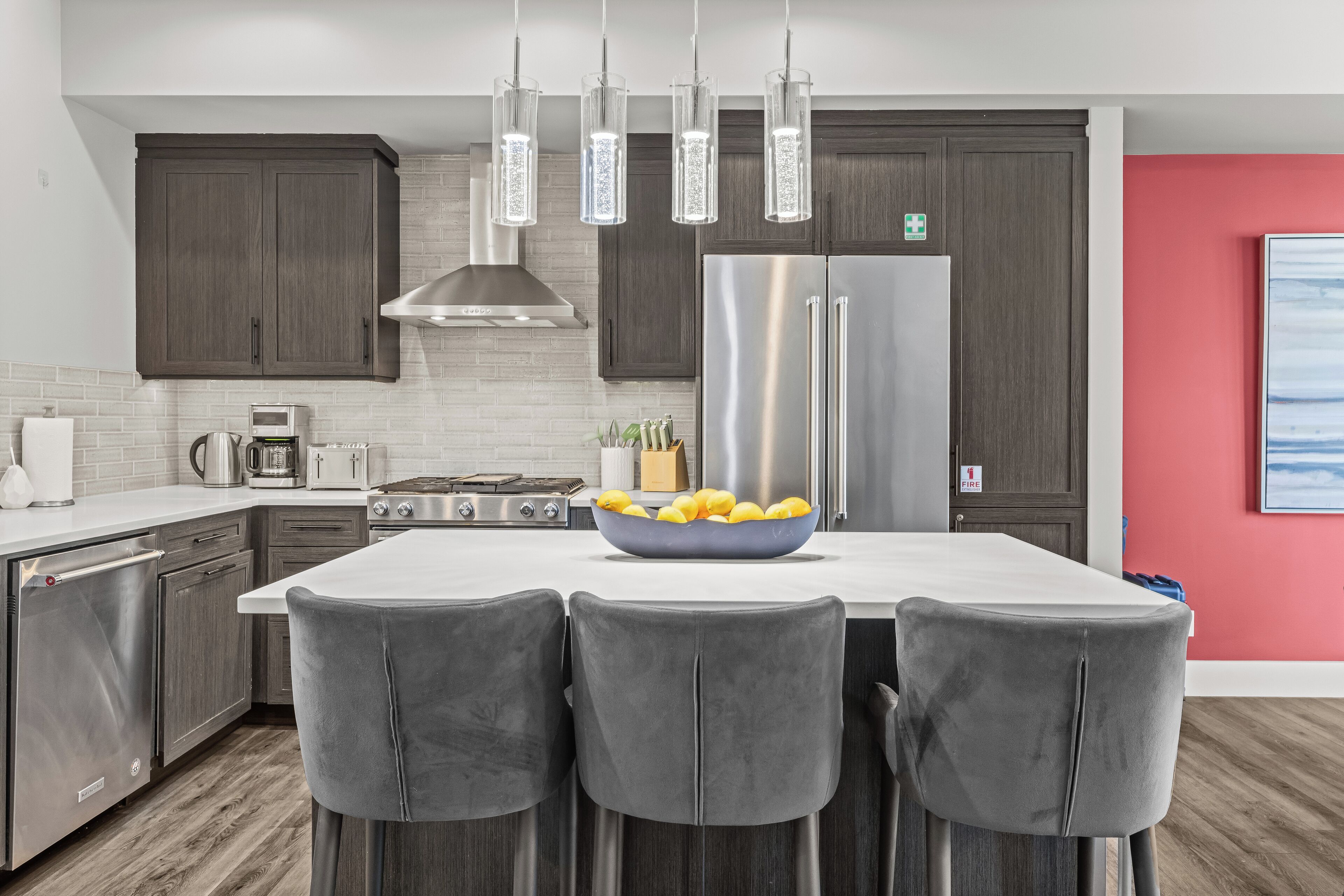 Una cocina moderna con armarios de madera oscura, electrodomésticos de acero inoxidable, una isla central con taburetes de bar e iluminación colgante.
