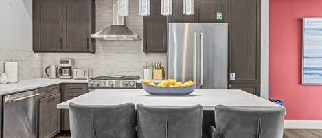 Una cocina moderna con armarios de madera oscura, electrodomésticos de acero inoxidable, una isla central con taburetes de bar e iluminación colgante.