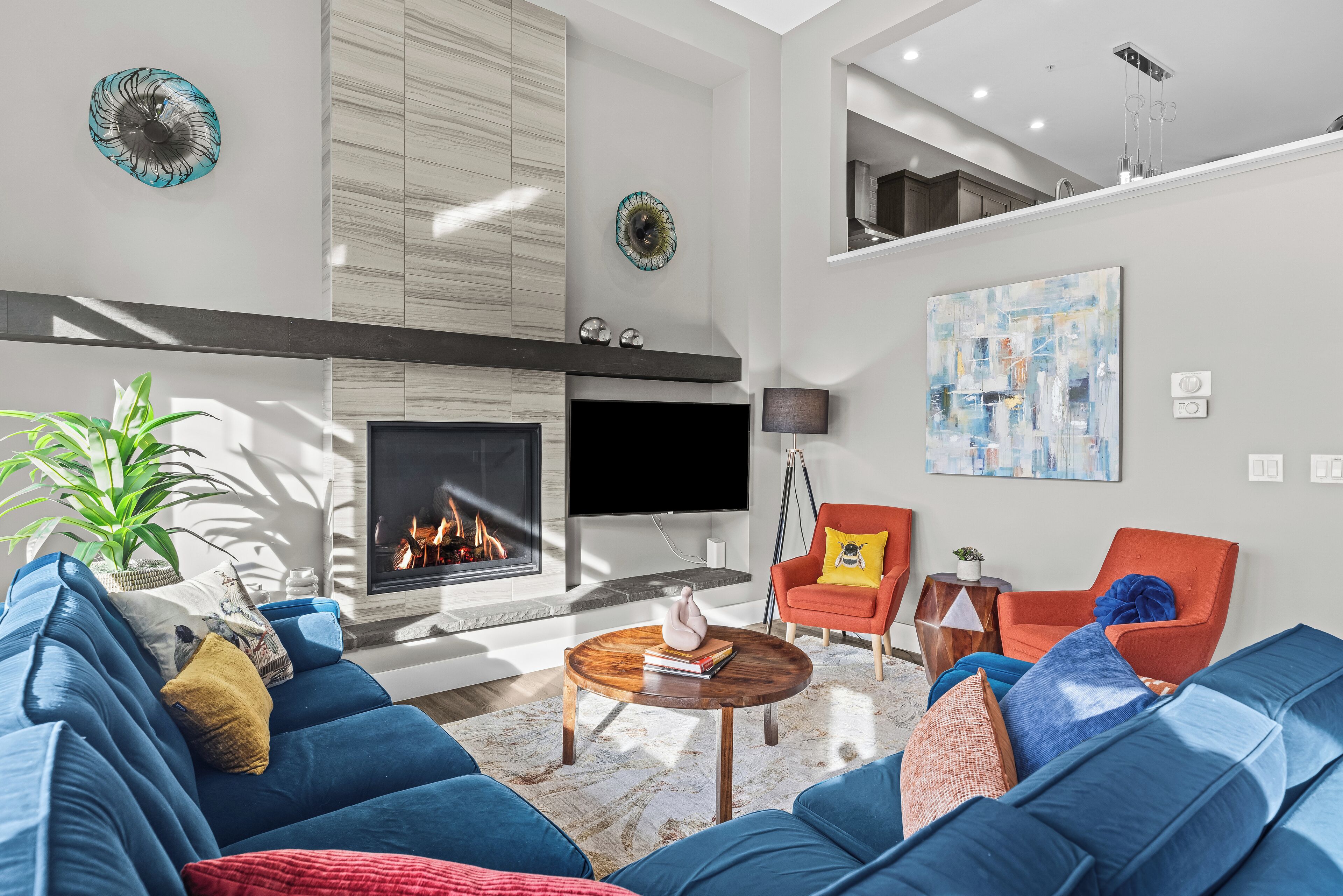 A modern living room with a fireplace, blue sofas, a coffee table, and a flat-screen TV.