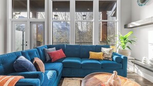 Un salón moderno con un sofá modular azul, una mesa de centro de madera y grandes ventanales con vistas a montañas.