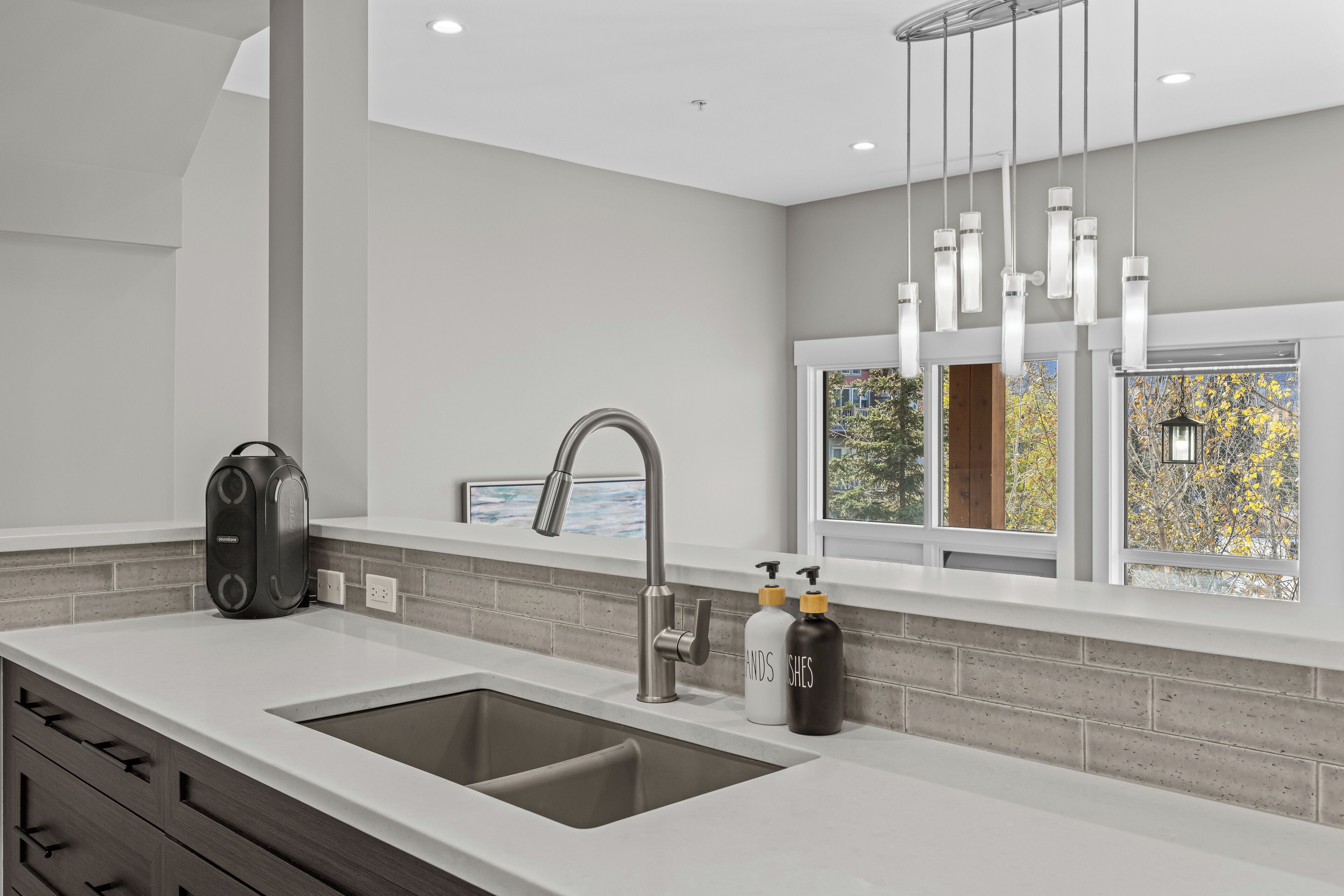 A modern kitchen with a double sink, a built-in range hood, and a window with a view of trees.