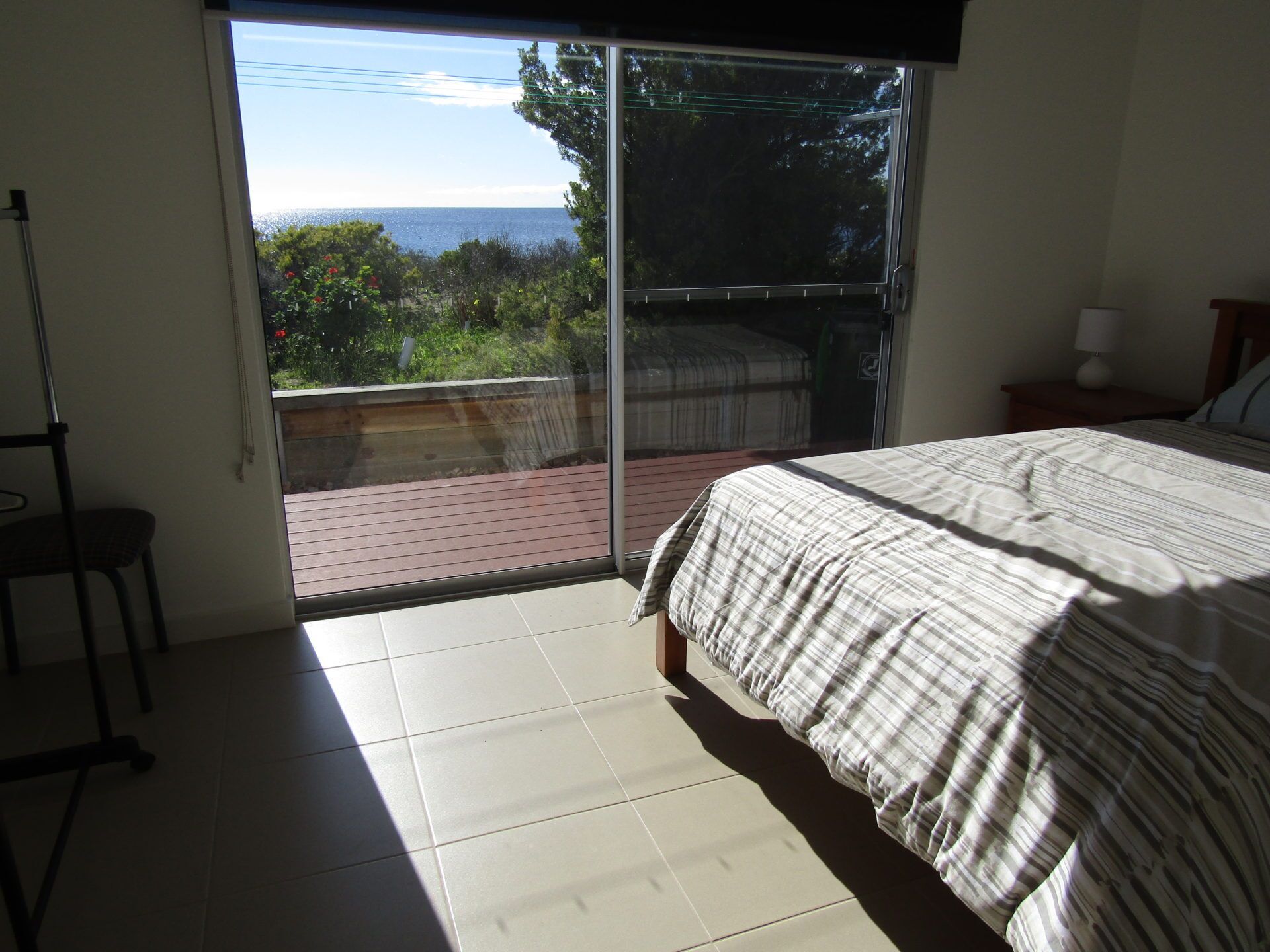 Ein Schlafzimmer mit Bett, Stuhl und Meerblick durch eine Schiebetür.