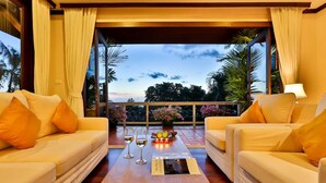 A room with two white sofas, a wooden coffee table with wine glasses and a menu, and a balcony with plants and a view of the sky. - Katamanda Kata View villa E5 near kata Noi Beach (Karon)