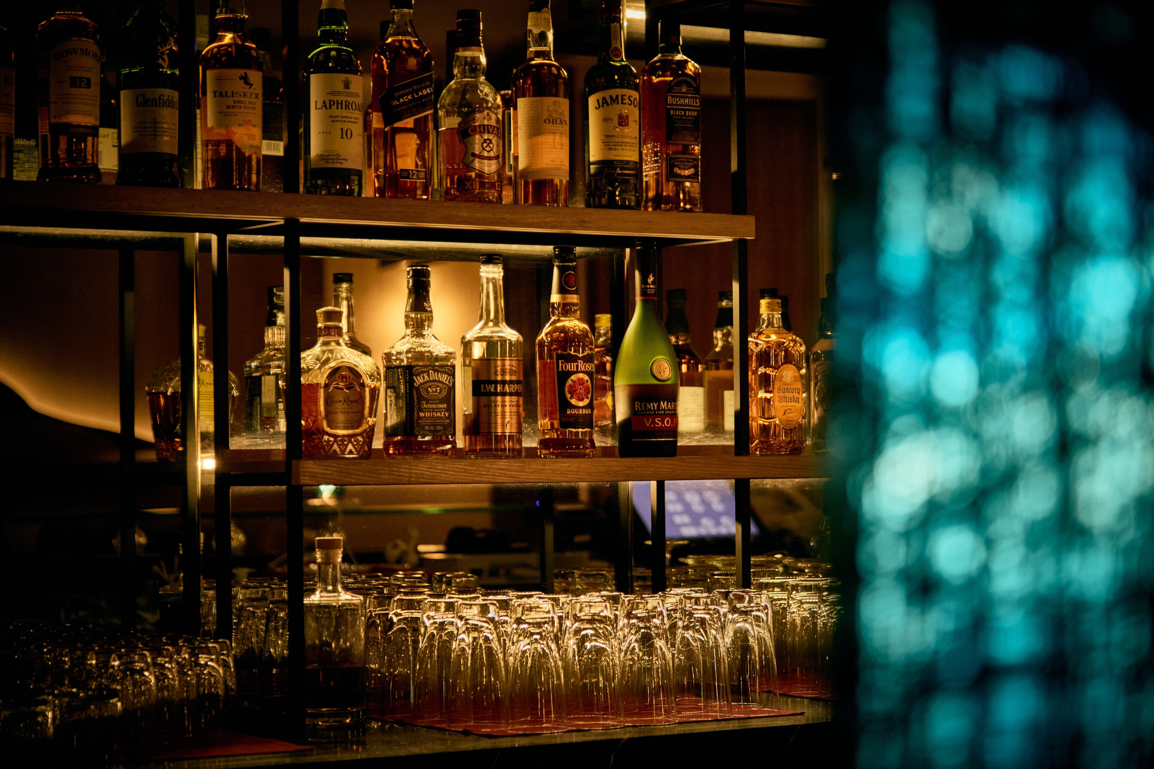 Un bar con estantes llenos de botellas de licor y numerosos vasos.