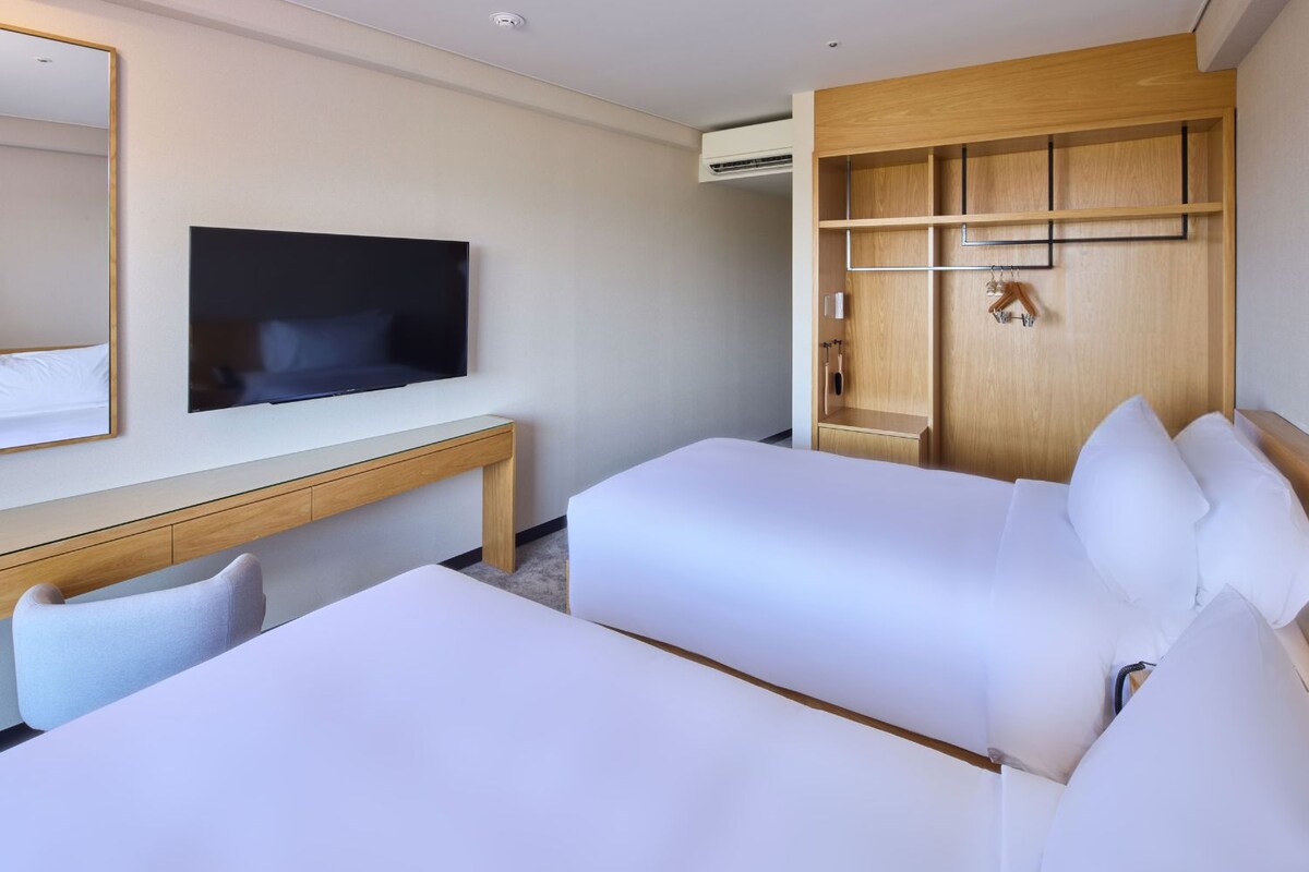 Ein Hotelzimmer mit zwei Betten, einem Schreibtisch, einem Fernseher und einem Holzschrank.