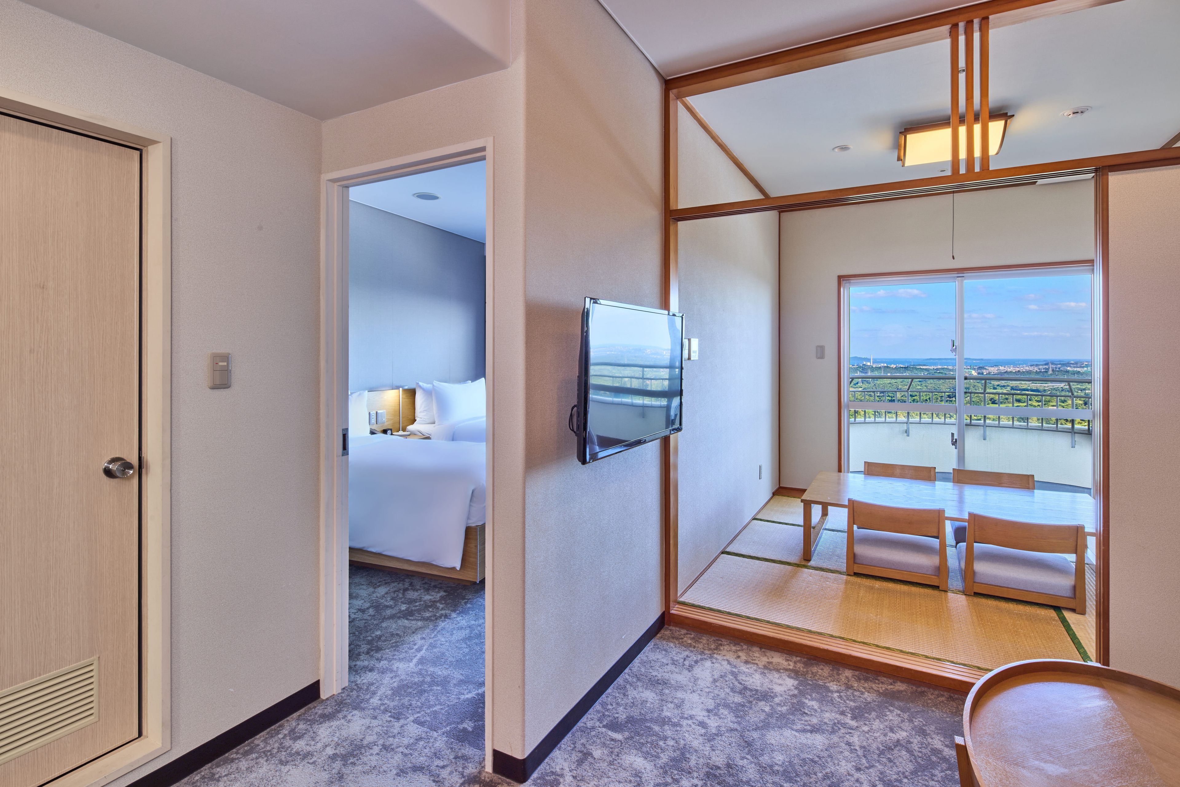 Une chambre d’hôtel avec un lit, un téléviseur fixé au mur, un balcon avec vue et une table en bois avec des chaises.