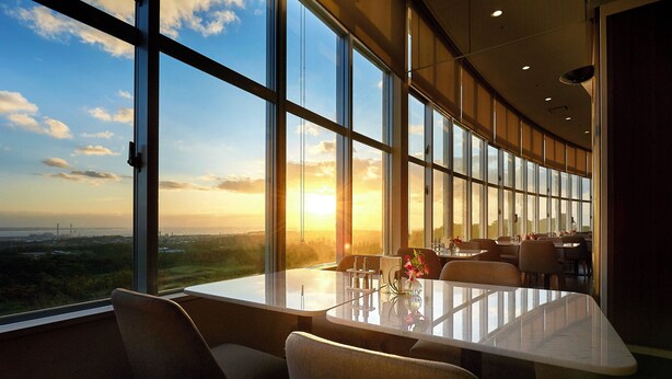 A restaurant with a large window offering a view of the sunset over a landscape. - ANA Crowne Plaza Resort Okinawa Uruma Hills by IHG (Uruma)