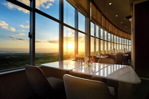 A restaurant with a large window offering a view of the sunset over a landscape. - ANA Crowne Plaza Resort Okinawa Uruma Hills by IHG (Uruma)