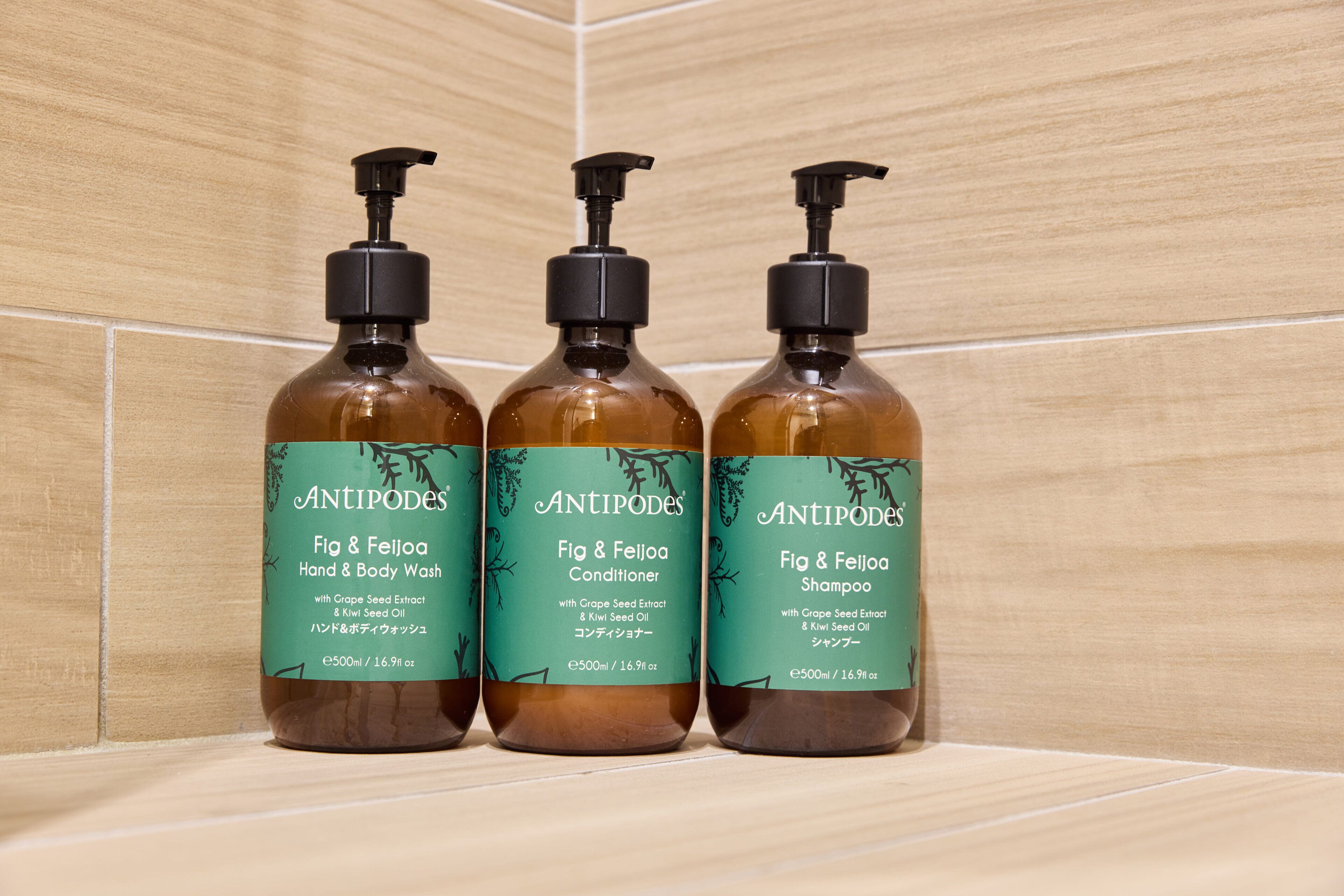 Three bottles of Antipodes Fig & Feijoa Hand & Body Wash, Conditioner, and Shampoo on a tiled shelf.