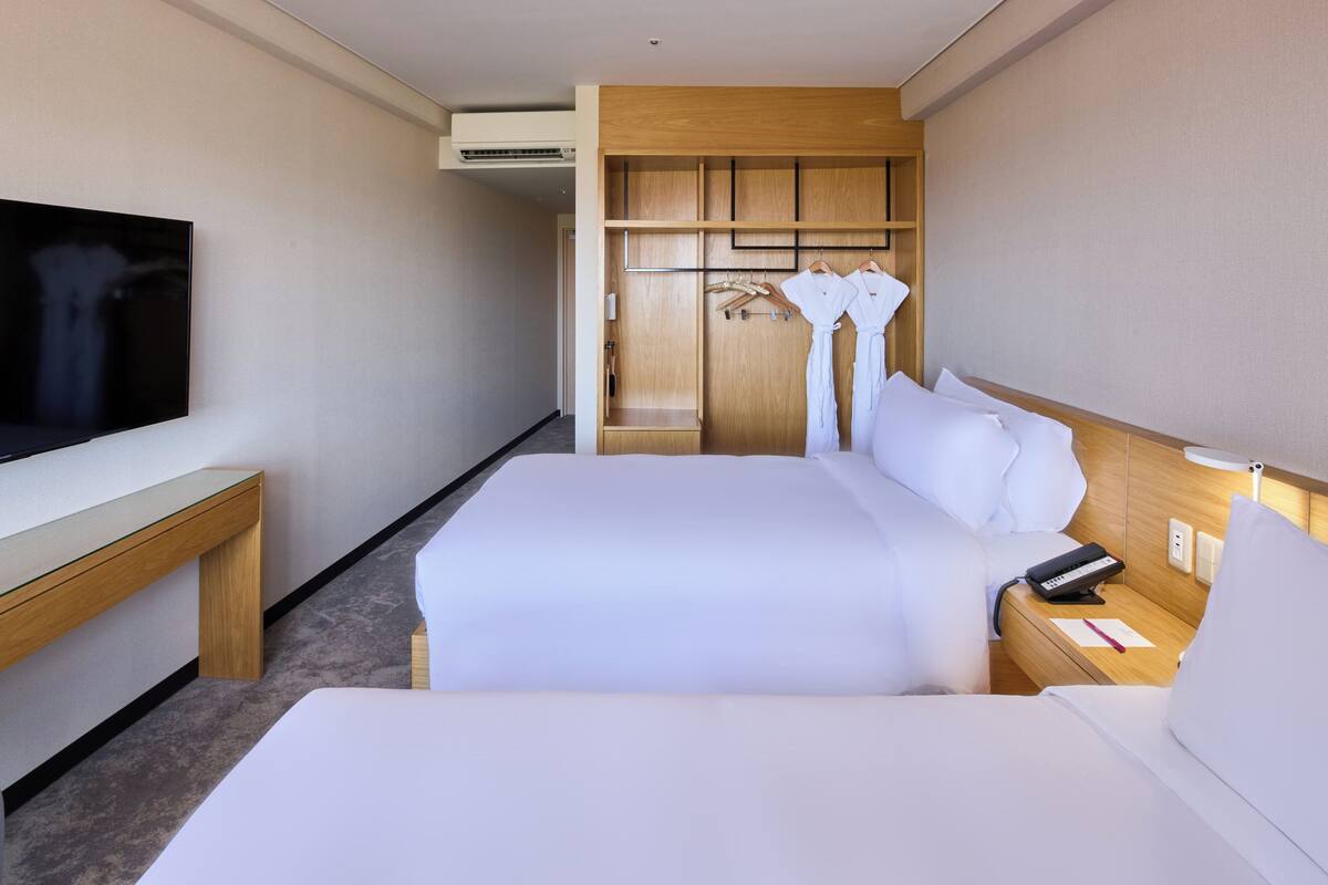 A hotel room with a large bed, a bedside table with a lamp, a TV, and a wooden wardrobe with hanging robes.