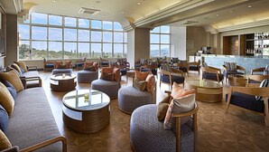 A spacious lounge area with multiple seating options, including sofas and ottomans, arranged around a central coffee table. Large windows provide a view of the outdoors. - ANA Crowne Plaza Resort Okinawa Uruma Hills by IHG (Uruma)