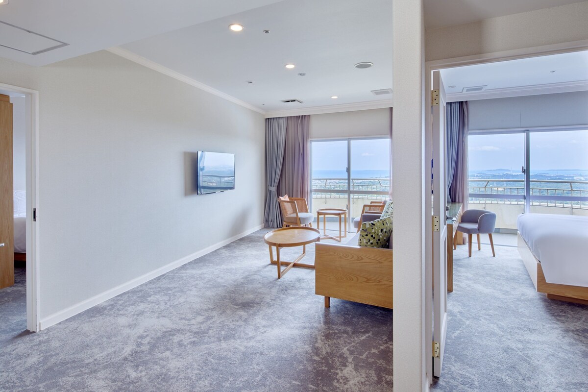 A hotel room with a bed, a TV, a balcony with a view, and a seating area with a table and chairs.