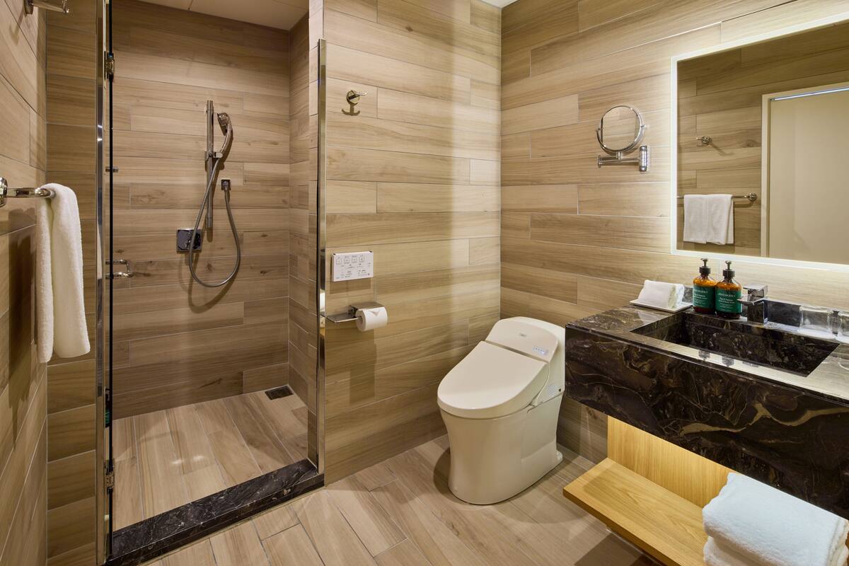A modern bathroom with a glass-enclosed shower, a toilet, a sink with a marble countertop, and a wooden vanity.