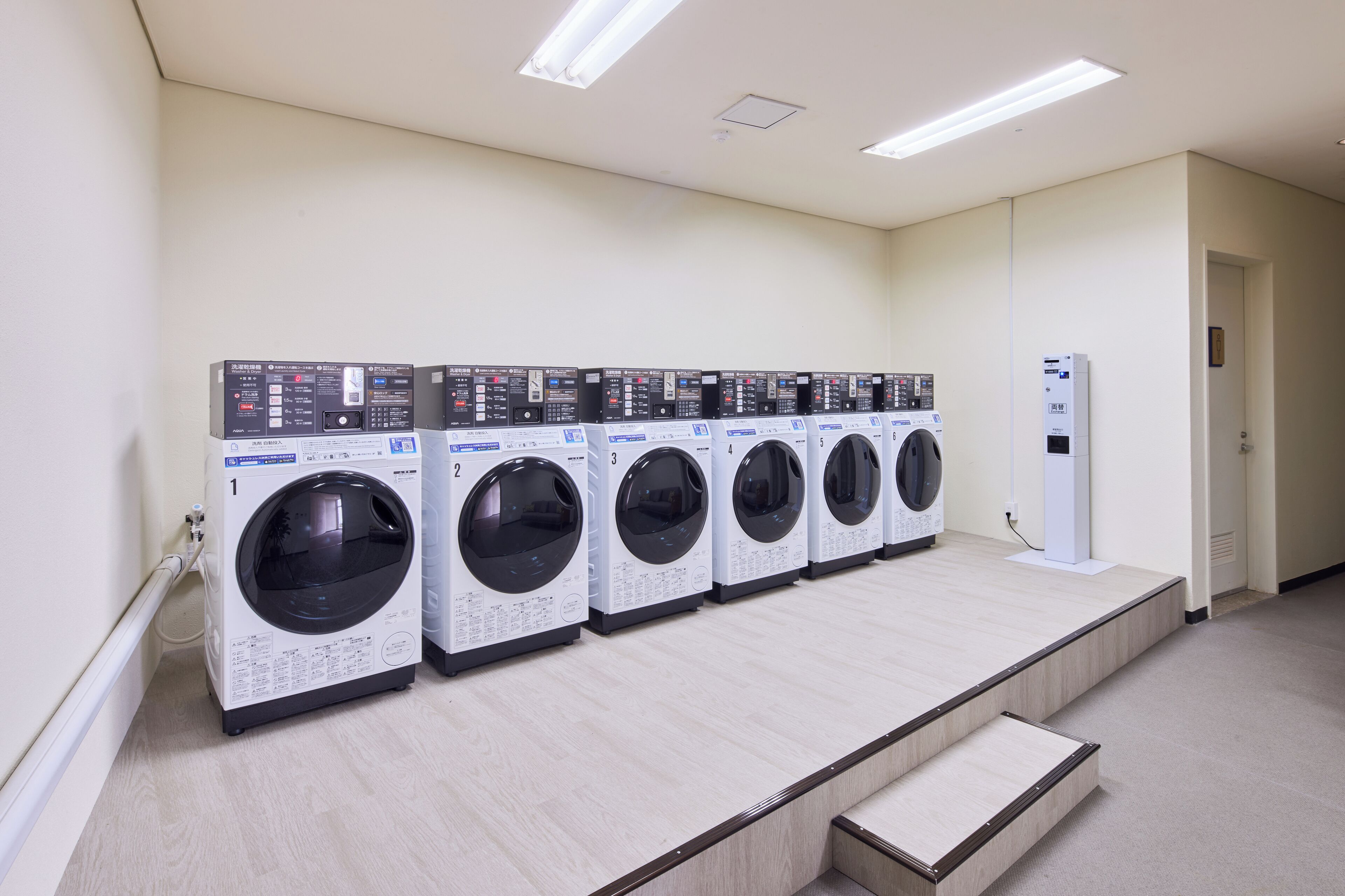 A laundry facility with five washing machines lined up against a wall.