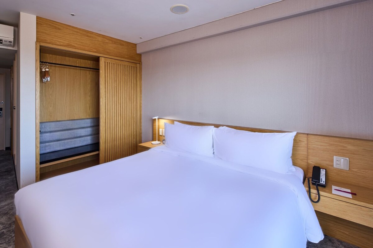 Ein Hotelzimmer mit einem großen Bett, einem hölzernen Kopfteil, einem Nachttisch mit Lampe, einem Telefon und einem Kleiderschrank.