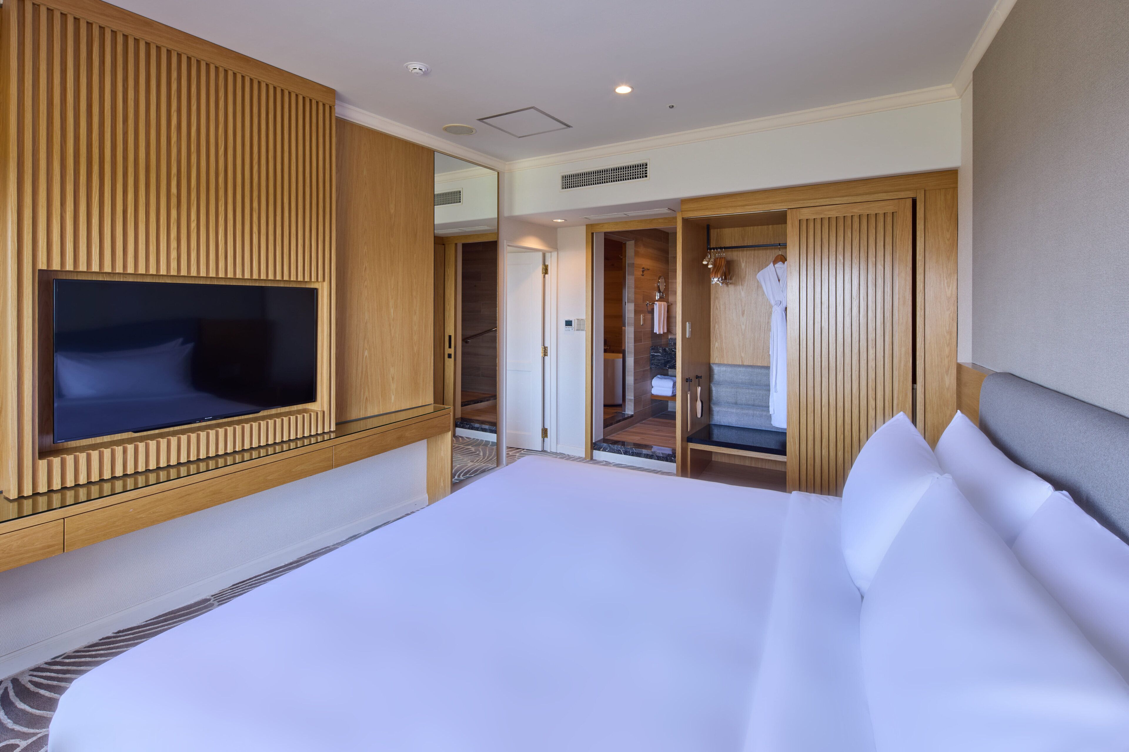 Une chambre d’hôtel avec un grand lit, un téléviseur fixé au mur, des boiseries et un dressing.