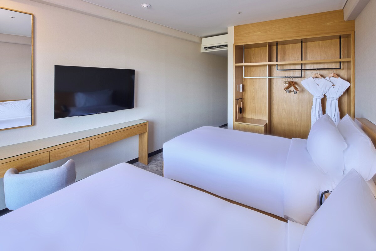 Ein Hotelzimmer mit zwei Betten, einem Fernseher, einem Holzschrank und einem Schreibtisch.