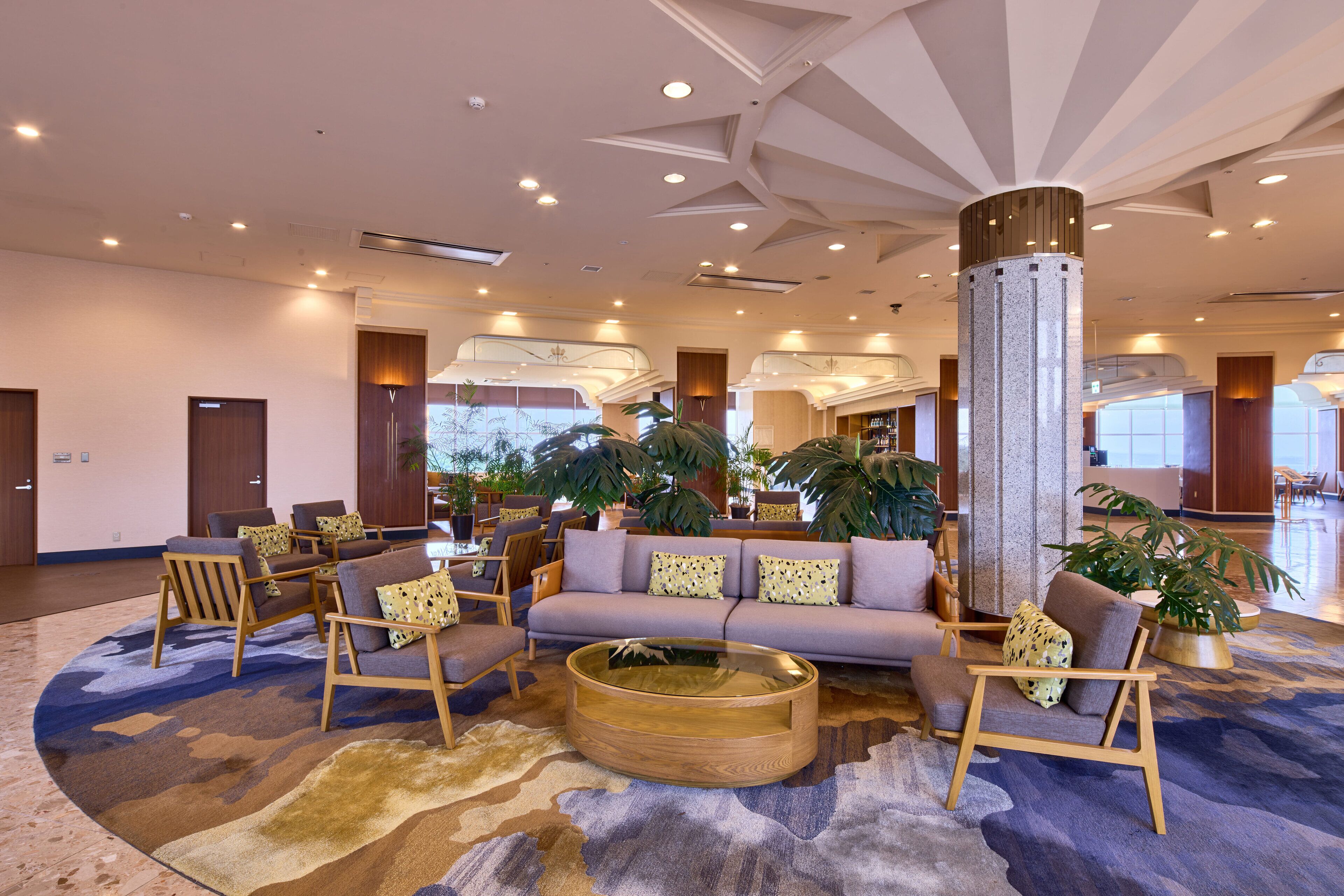 A spacious lobby with a round coffee table, sofas, and chairs arranged around a central pillar.