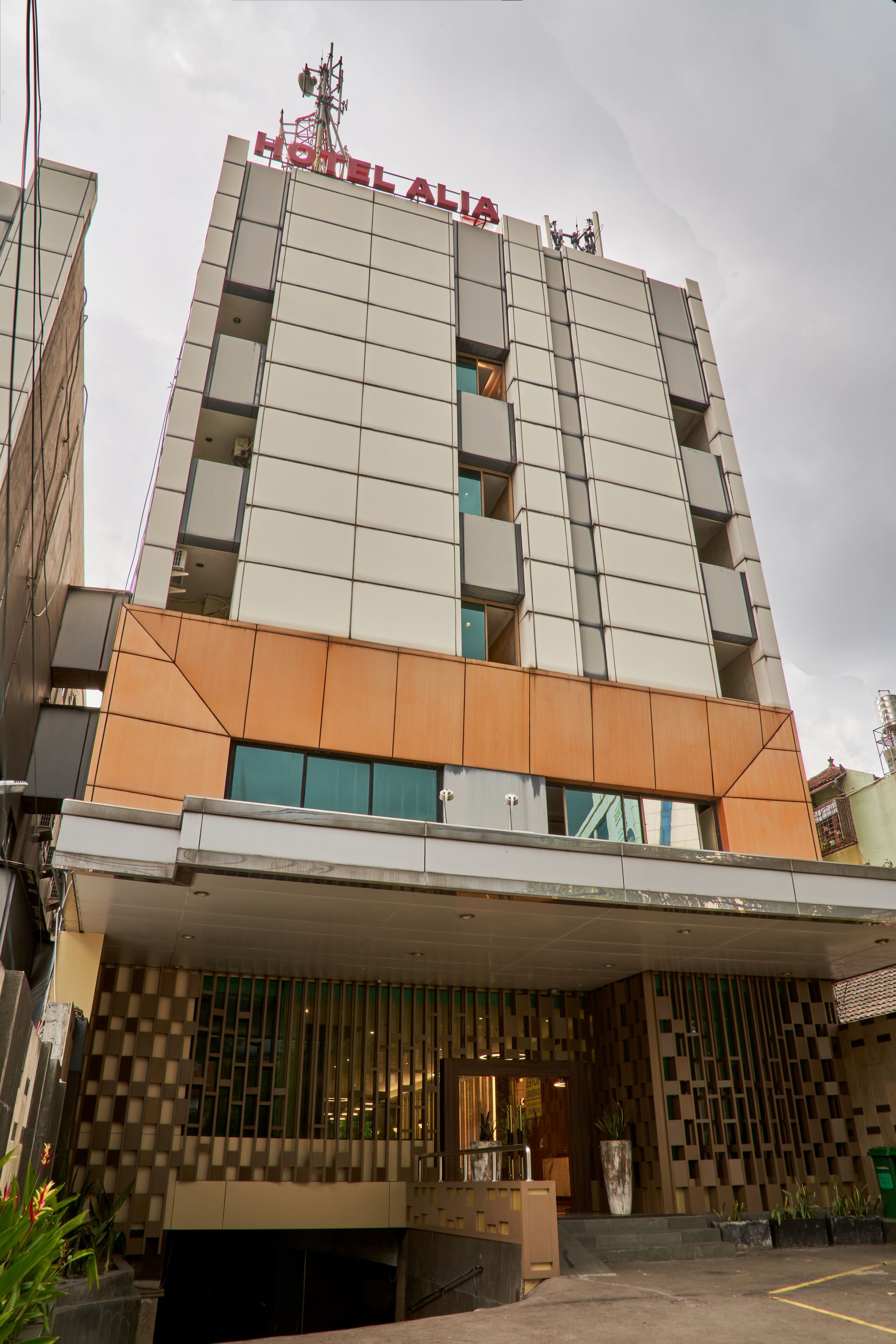 A hotel with a modern facade, a prominent sign at the top, and a covered entrance with a patterned wall.