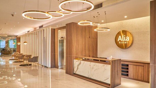 A modern hotel reception area with a marble counter, wooden paneling, and circular ceiling lights. - Alia Boutique Pasar Baru (Jakarta)