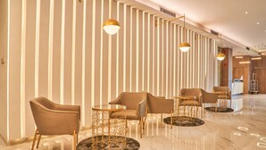 A modern hotel lobby with a sleek design, featuring a row of sofas and round tables with gold accents, a marble floor, and vertical light fixtures. - Alia Boutique Pasar Baru (Jakarta)