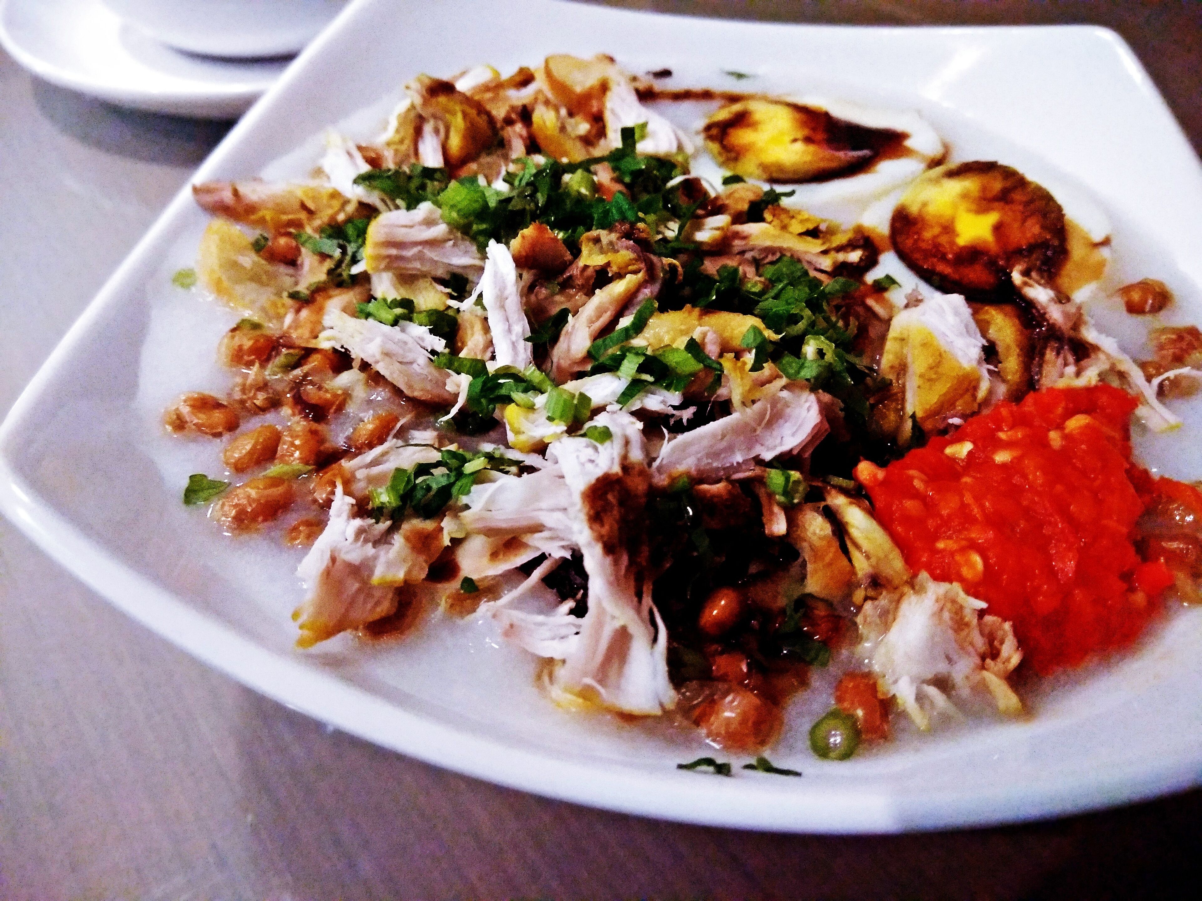 A plate of shredded chicken with vegetables and a dollop of sauce.