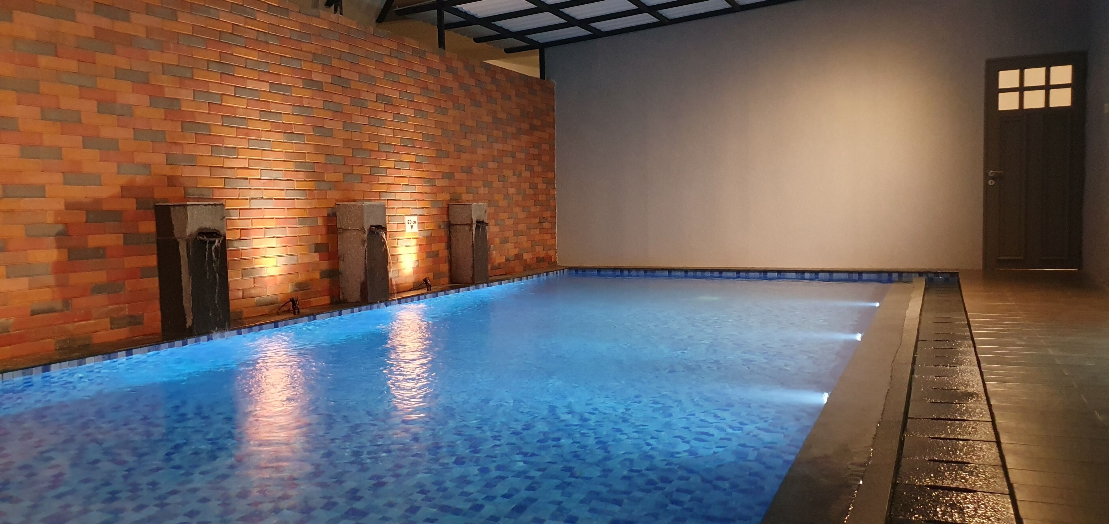 Une piscine dont le sol et les murs sont recouverts de carreaux, avec une porte et un plafond orné d’un motif en réseau.