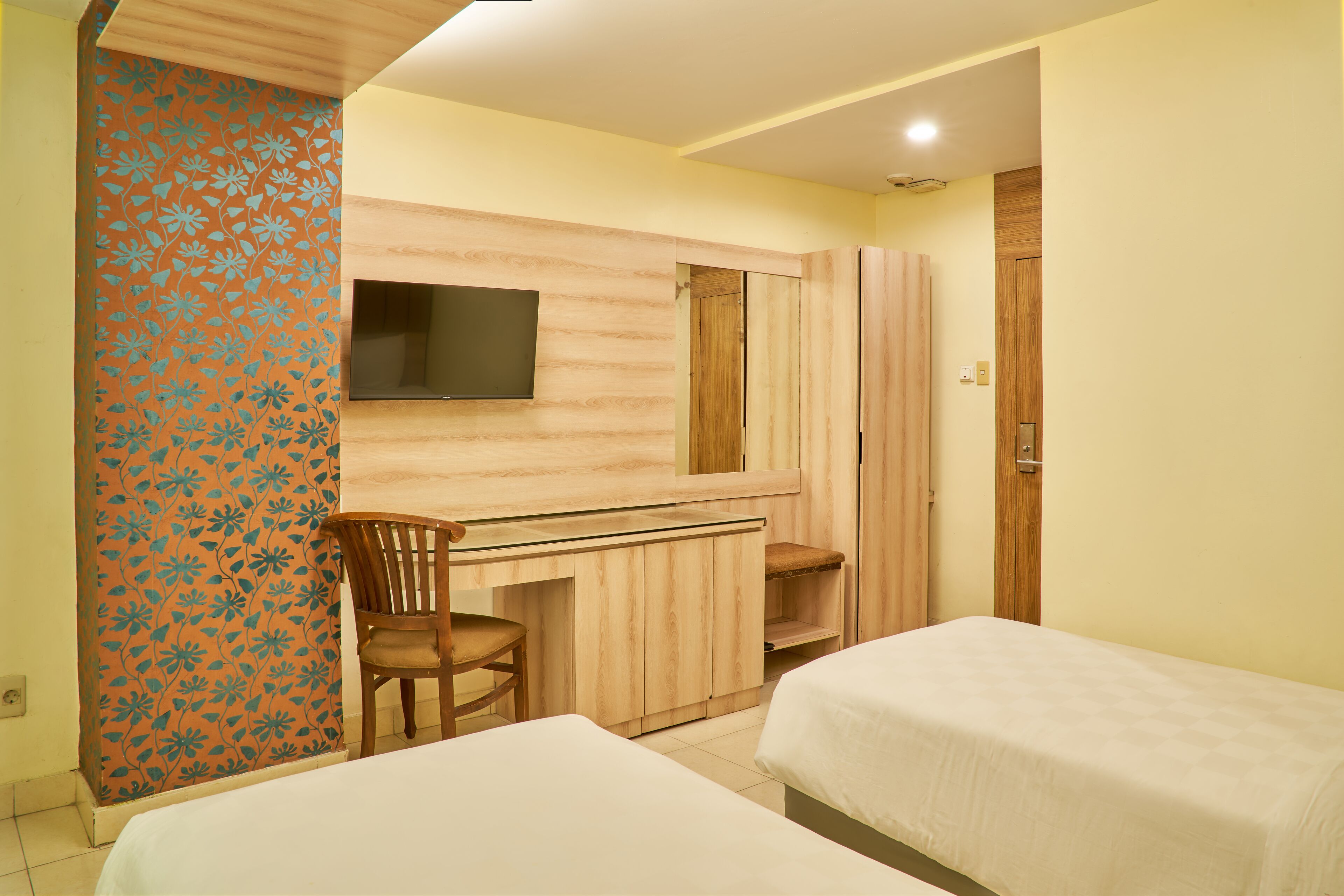 Ein Hotelzimmer mit zwei Betten, einem Schreibtisch mit Stuhl, einem an der Wand montierten Fernseher und einem Kleiderschrank.