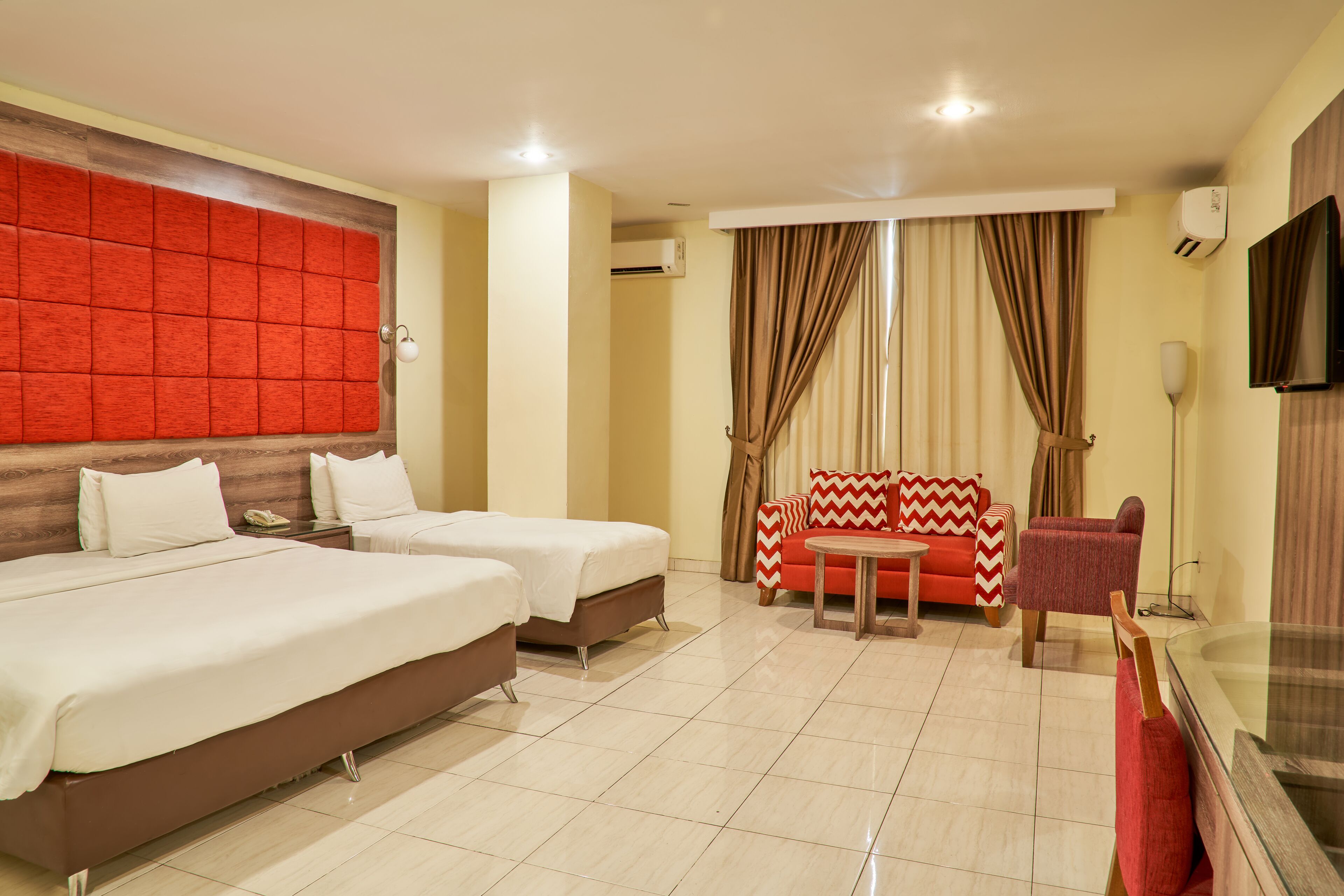 A hotel room with two beds, a sofa, a small table, and a TV.
