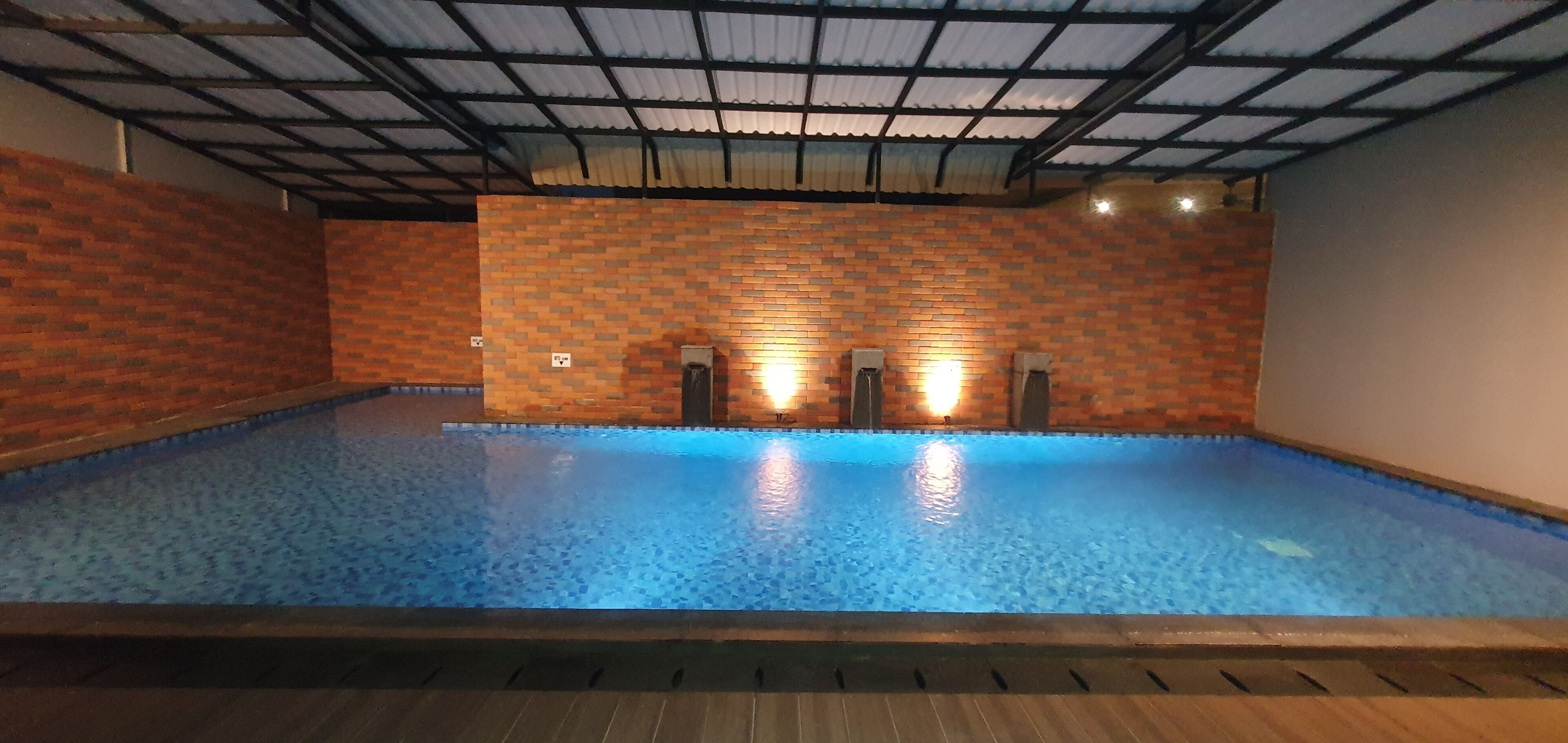 Ein Hallenbad mit Fliesenboden und -wänden, umgeben von einer Ziegelmauer und einer Metall-Dachkonstruktion.