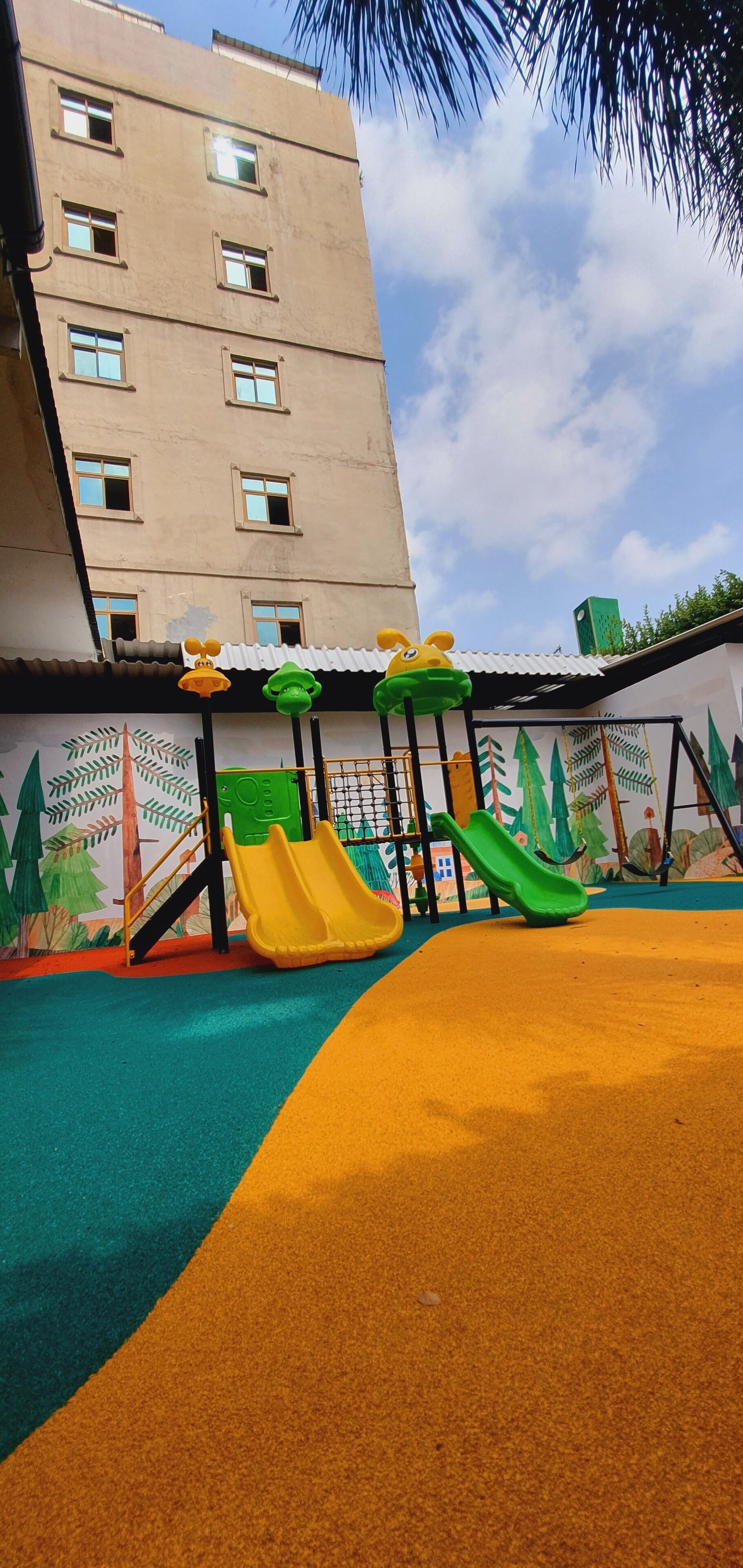 Un parc infantil amb tobogans i una estructura per escalar, tot envoltat d'un edifici amb nombroses finestres.